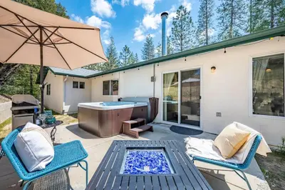 a patio with a tub and two chairs and an umbrella at Manic Mountain Forest Cabin 3 miles from Bass Lake in Oakhurst