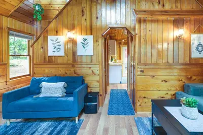 a living room with a blue couch and wooden walls at Fire Pit, Deck and Grill Cozy Twain Harte Cabin! in Twain Harte