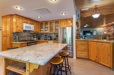 a kitchen with wooden cabinets and a large island with bar stools at Yosemite Creekside Retreat with spa/games/EV Charger and more in Oakhurst