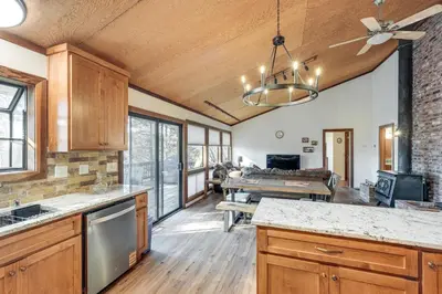 a kitchen with wooden cabinets and a living room at Deck and Gas Grill Secluded Arnold Cabin Rental! in Arnold