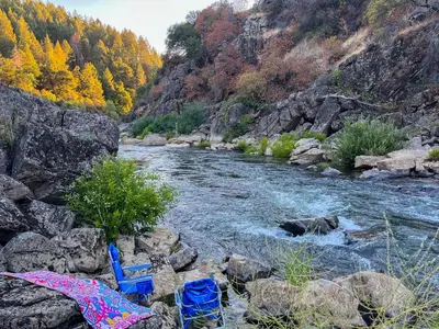 a river with two blue chairs sitting on the rocks at Meadow Vista Mountain Escape with River Views! in Meadow Vista