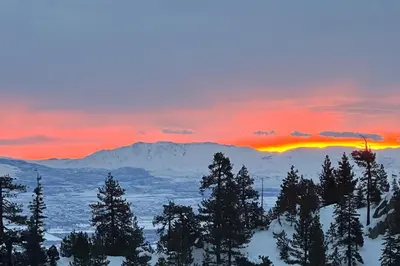 a sunset over a snowy mountain with trees in the foreground at Sunrise Serenity at Tahoe Village in Stateline
