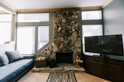a living room with a tv and a stone wall at BEST Location . Walk To Canyon Lodge . Views . Pool/Spa in Mammoth Lakes