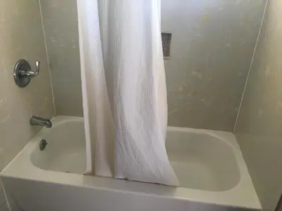 a bathroom with a white shower curtain next to a tub at Valley Motel in Atwater