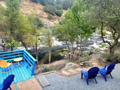 a blue bench with chairs and a table next to a river at Retro House on the River ! in Three Rivers
