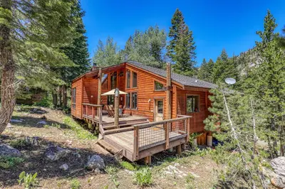 a log cabin in the woods with a wooden deck at Alpine Escape by Tahoe Getaways - Shuttle to Ski Slopes & Fireplace in Alpine Meadows