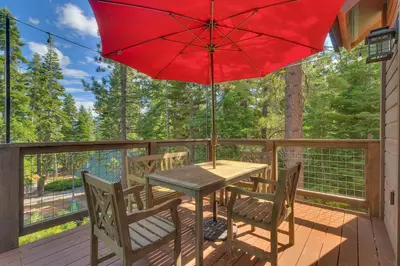 a table and chairs on a deck with a red umbrella at Bluebird Lodge by Tahoe Getaways - 4 BR with Hot Tub, Pool Table & Lake Views in Carnelian Bay