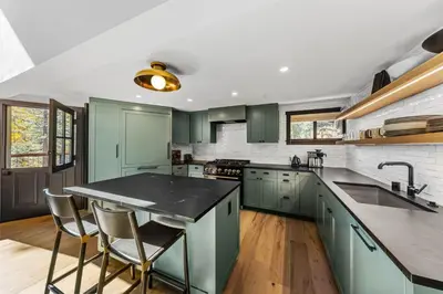 a kitchen with green cabinets and a kitchen island with chairs at Birchwood Retreat by Tahoe Getaways - Newly Remodeled Pet Friendly Home in Alpine Meadows with Wood Fireplace, Hot Tub & Ski Shuttle! in Alpine Meadows