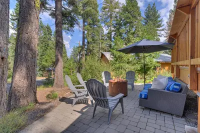 a patio with chairs and an umbrella and a couch at Blackwood Bungalow on the West Shore by Tahoe Getaways - 3 BR Pet Friendly & Walking Distance to the Lake in Homewood