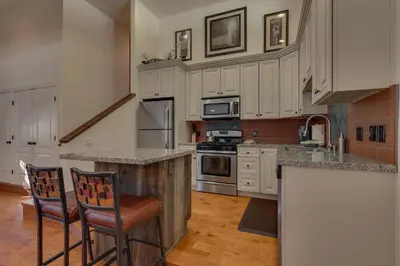 a kitchen with white cabinets and a island with two chairs at Glades Getaway by Tahoe Getaways - Charming Pet-Friendly 3 BD North Shore Cabin w Wood Fireplace & Short Drive to Ski Resorts in Carnelian Bay