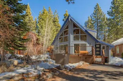 a home in the woods with a wrap around porch at Moon Dune Chalet by Tahoe Getaways - Remodeled 3 BR Cabin plus Loft w Fenced Yard & Walk to Beach or Dining in Tahoe Vista