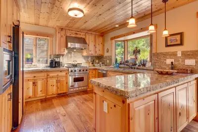 a large kitchen with wooden cabinets and a large island at Tippy Canoe by Tahoe Getaways - 4BR West Shore w Private Hot Tub,, Sauna, EV & Walking Distance to Trailhead in Tahoma
