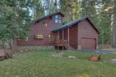 a large wooden house in the middle of a yard at Dogwood Place by Tahoe Getaways - 3BR Pet-Friendly Tahoe Donner Home w Hot Tub, Pool Table, Wood Fireplace & HOA Amenities in Truckee
