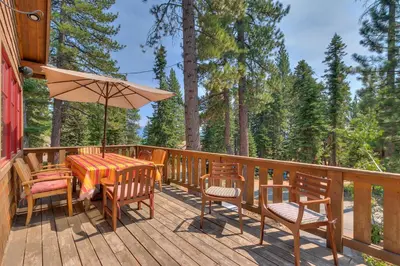 a deck with a table and chairs and an umbrella at Mountain Escape at North Shore - Upscale 4BR Easy Walk to Lake & Private Hot Tub! in Carnelian Bay