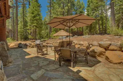 a table and chairs with an umbrella on a stone patio at New Listing! West Shore Bliss - 4BR, Private Hot Tub in Tahoe City