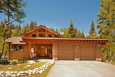 a wooden house with a garage in the woods at Creek Side- 4 Primary Suites, Hot Tub, Shuttle to Slopes, Pet Friendly in Olympic Valley