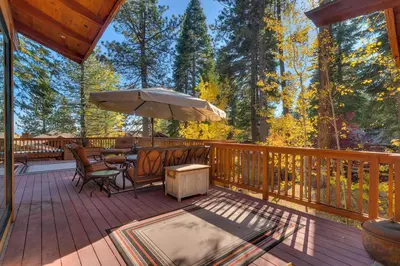 a deck with a table and chairs and an umbrella at Gray Bear Lake View Estate - Stunning Cabin w 4 Master Suites, Private Hot Tub! in Carnelian Bay