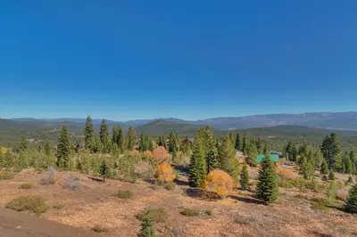 an open field with trees and mountains in the background at Grand Vista Lodge by Tahoe Getaways - 5 BR with Stunning Views, Pool Table, Private Hot Tub & HOA Pool! in Truckee