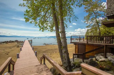 a wooden walkway to the beach with a house at Lakeside Escape - Beautiful Lakefront, Pier, Wood Fireplace, Private Hot Tub in Tahoe Vista