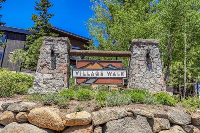 a village walk sign in front of a stone wall at Larkspur Luxe at Northstar- 4 BR with Pool, Gym, Access - Walk to Village, Private Hot Tub in Truckee