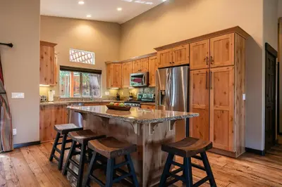 a kitchen with wooden cabinets and a large island with bar stools at Pinecrest at Winter Creek- Cozy Cabin w Hot Tub, Walk To Downtown Truckee in Truckee
