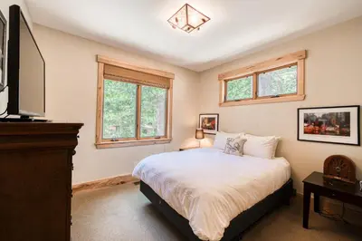 a bedroom with a bed and a tv and windows at Truckee Timbers at Gray's Crossing by Tahoe Getaways - 4BR w Hot Tub, Ping Pong & EV in Truckee