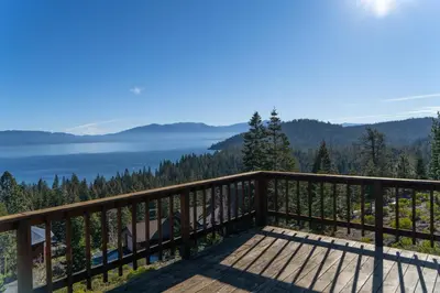 a wooden balcony with a view of a lake at Sierra Lake View at Rubicon by Tahoe Getaways - 3 BR, Panoramic Lake Views, Private Hot Tub & Private beach! in Tahoma