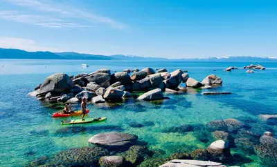 two people on surfboards in the water near rocks at VIP Lakefront Condo Amazing Views Pool Pickleball Excellent Location Balcony BBQ in Kings Beach
