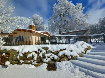 a house covered in snow with a stone wall at Yosemite Gateway Cottage - King Suite - Mountain Views in Oakhurst