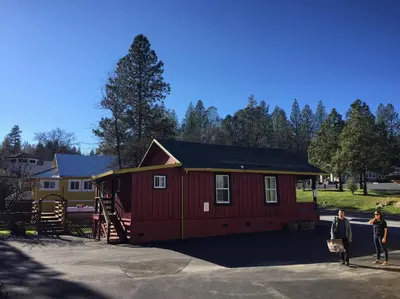 a small red house with a staircase and two people standing outside at Yosemite International Hostel in Groveland