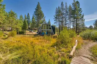 a building in the middle of a field with trees at Modern Gambrel Cabin Near Ski Resorts in Truckee