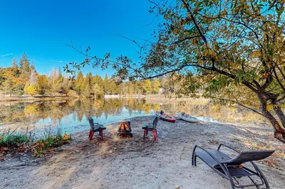 three chairs sitting around a fire next to a lake at 1BR Dog-Friendly Lakefront Cabin with Canoes in Twain Harte