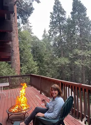 a woman sitting on a deck with a fire pit at A-Frame Cabin in The Sequoias in Wofford Heights
