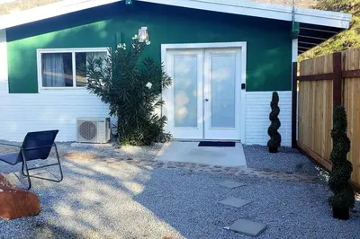 a green house with a white door and a fence at Retro Casita on the River! only 1 min to SNP gate! Riverfront with swimming in Three Rivers