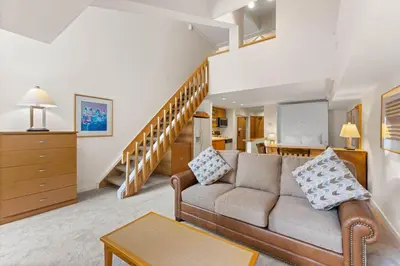 a living room with a couch and a staircase at Palisades Tahoe Lodge Rentals Studio Loft #310 in Olympic Valley