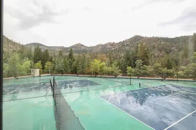 a tennis court with turquoise water and mountains in the background at Palisades Tahoe Lodge Rentals Studio Loft #329 in Olympic Valley