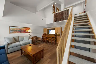 a living room with a staircase with a couch and a table at Palisades Tahoe Lodge Rentals Studio Loft #329 in Olympic Valley