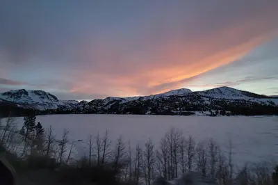 a sunset over a lake with snow covered mountains at Lakefront Mountain Retreat in June Lake