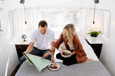 a man and woman sitting on a bed looking at a map at AutoCamp Sequoia in Three Rivers
