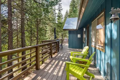 a deck with two green chairs on a blue house at Starlight Cabin in Oakhurst