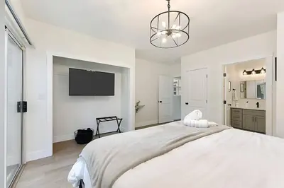a white bedroom with a large bed and a flat screen tv at East Sac Getaway, Walking Distance to Hospitals in Sacramento