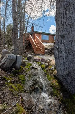 a house in the woods with a creek in front at Mineral Springs 3 BR w Hot tub Available in Alpine Meadows in Olympic Valley