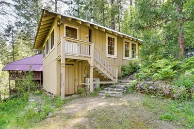 a yellow house in the middle of the woods at 8 Mi to Yosemite National Park Cabin with Fire Pit in Oakhurst