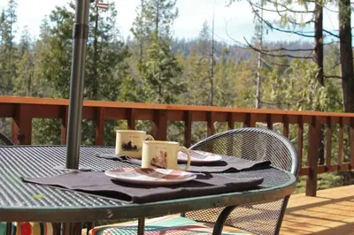 a table on a deck with two mugs on it at Baxter Mountain Cottage in Shaver Lake