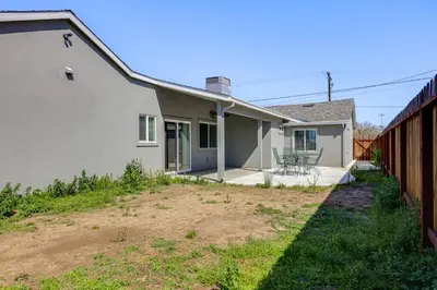 a white house with a fence next to a yard at Quaint Hughson Vacation Rental, Walk to Downtown! in Hughson