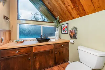 a bathroom with a toilet and a sink and a window at Bass Lake Chalet- A frame with hot tub/firepit in Oakhurst