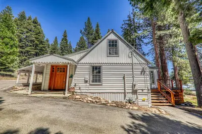 a white house with a red door in the woods at Reflections Lakeview Cabin - Private Beach Access, Hot Tub & Buoy! in Carnelian Bay