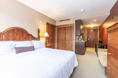 a bedroom with a large white bed and a kitchen at Catamount Lodge 201 by East West Hospitality in Truckee