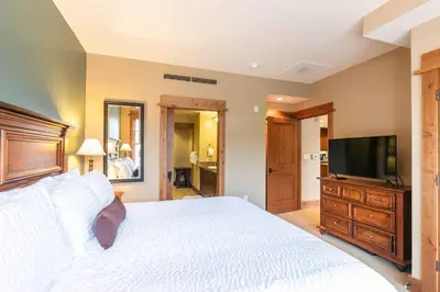a bedroom with a white bed and a flat screen tv at Catamount Lodge 201 by East West Hospitality in Truckee