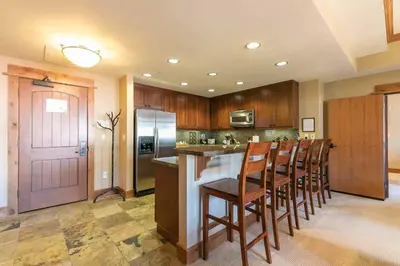 a kitchen with wooden cabinets and a bar with chairs at Catamount Lodge 301 by East West Hospitality in Truckee
